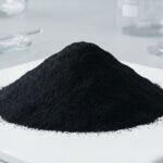 A mound of fine black iron oxide pigment powder in a laboratory, used for coloring plastics and rubber applications.